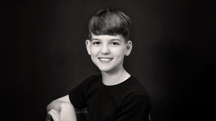 A studio portrait of a brown-eyed cute boy, smiling teenager in black clothes on a black...
