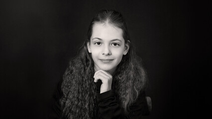 Portrait of a smiling beautiful  brown-haired girl with wavy hair, in black clothes on a black...