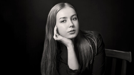Portrait of a beautiful young blonde with straight long hair and blue eyes, in black clothes on a...