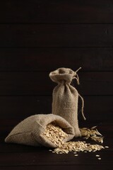 Oat flakes and sacks on dark wooden table against black background