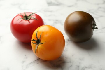 Different ripe tomatoes on white marble table, closeup