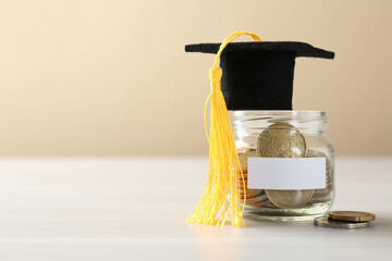 Scholarship. Jar with graduate hat and coins on white wooden table, closeup. Space for text