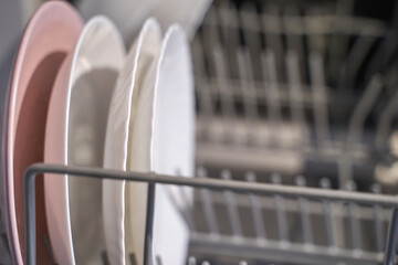 Close up of clean plates in dishwasher rack with soft focus on kitchenware interior organization.