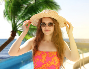Girl with straw hat and sunglasses in swimming pool at sea resort