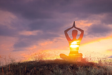 Practicing yoga in nature. Woman meditating in lotus position on hill. Double exposure with sunset...