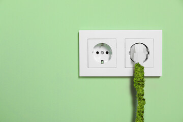 Electricity and nature. Power plug in socket on light green wall. Wire of power plug covered with...
