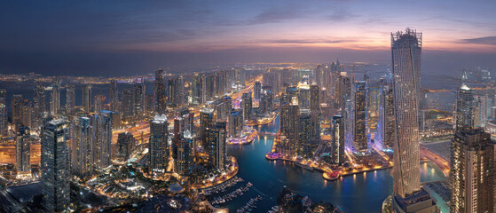 Fototapeta premium Panoramic aerial view of a futuristic city skyline at dusk, featuring illuminated skyscrapers, waterways, and vibrant urban infrastructure. 