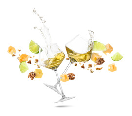Glasses with splashing wine, cheese cubes and walnuts in air against white background