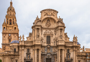 Stunning facade of Murcia Cathedral in Spain, showcasing intricate Baroque architecture, detailed sculptures, and historical charm under a cloudy sky