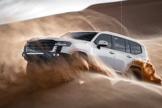 White SUV driving through desert sand, Saudi Arabia - Powered by Adobe