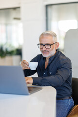Mature Businessman drinking coffee on laptop waiting for meeting to start, making business decision.