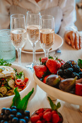 Brunch and bubbly celebration. Friends gather around a dining table to enjoy fresh fruits, salad, and sparkling beverages in a bright setting.