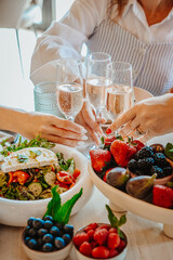 Brunch toast celebration. Friends raise their glasses in a toast while enjoying a fresh salad and a variety of fruits at a cheerful brunch.