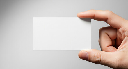 Fototapeta premium A hand holding a blank white rectangular card, ready for custom text or design, against a simple light background.