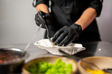 Chef in black gloves plating gourmet food in a professional kitchen. Culinary preparation with fresh ingredients, hygiene, and attention to detail.