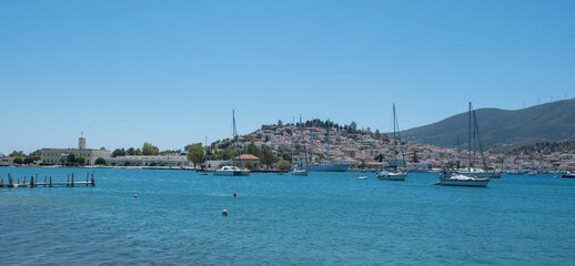 Poros Island harbor Greece. Boats on calm blue water, traditional architecture hillside houses and summer sky