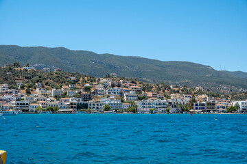 Fototapeta premium Poros Island panoramic view, Greece. Boats on calm blue water, traditional architecture hillside houses and summer sky