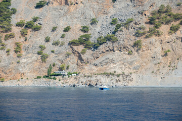 A white sailboat floats upon calm blue waters near the rugged rocky coastline of Agia Roumeli...