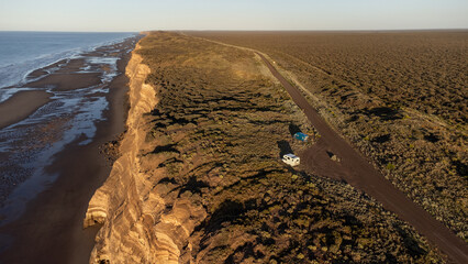 Two camper vans parked on a remote dirt road atop dramatic coastal cliffs, overlooking the vast...