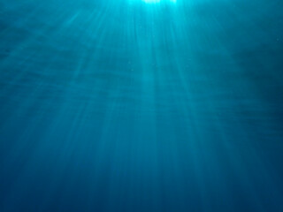 Dark blue ocean surface seen from underwater. Abstract waves underwater and rays of sunlight shining through, Sun light rays undersea deep, Underwater background with sea bottom, Mediterranean sea.