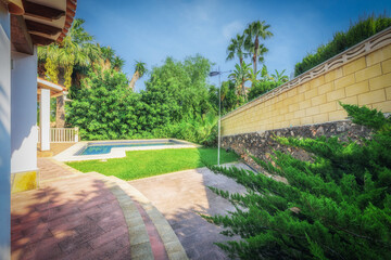 View from the terrace of the pool with a lawn surrounded by green plants.