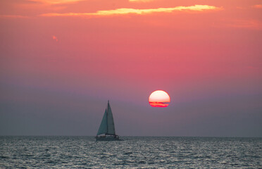 Sailboat at sunset over the sea in pink and orange tones