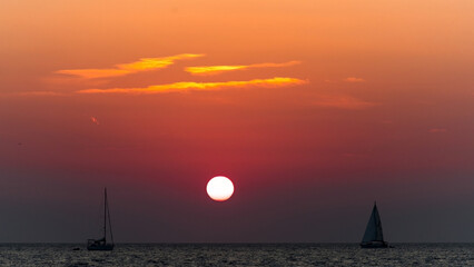 Sunset with two sailboats on the sea in orange and red tones