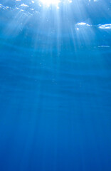 Dark blue ocean surface seen from underwater. Abstract waves underwater and rays of sunlight shining through, Sun light rays undersea deep, Underwater background with sea bottom, Mediterranean sea.