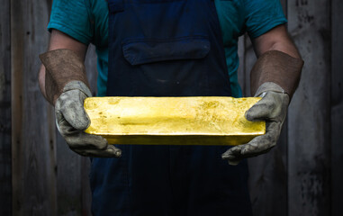 Gold bar. A dirty worker holds a large gold bar in his hands, realistic photo.