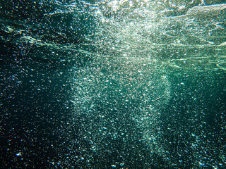 Dark blue ocean surface seen from underwater. Abstract waves underwater and rays of sunlight shining through, Sun light rays undersea deep, Underwater background with sea bottom, Mediterranean sea.