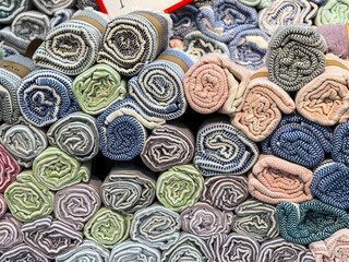 Rolled fabrics with striped patterns stacked in a market stall. Textile, furnishing and consumer choice expressed through material, comfort and lifestyle essentials.
