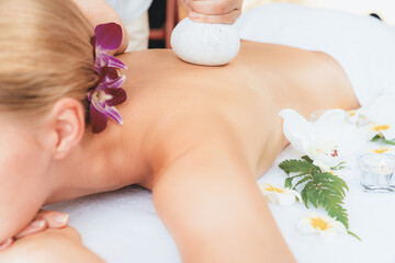 Closeup hot herbal ball spa massage body treatment, masseur gently compresses herb bag on woman...