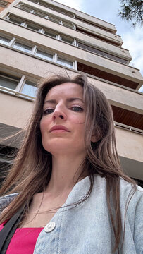 Brunette woman with blue eyes taking a selfie from below, low angle portrait with natural light. Casual lifestyle photo.