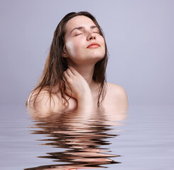 Beautiful young woman with perfect skin against grey background. Her reflection in rippled water