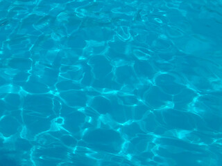 Blue water surface with sunlight reflections in a swimming pool. Leisure, recreation and summer lifestyle represented through clarity, refreshment and aquatic relaxation.