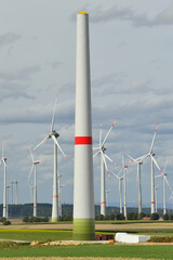 Wind farm with wind turbines, one of which is unfinished and currently under construction, while...