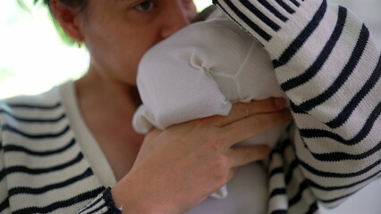 Mother gently lifts newborn close, checking the baby's diaper by smelling it to see if he pooped. a...