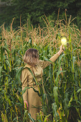 Young woman holding oval mirror with reflection of sun and looking at herself on corn field. Close...