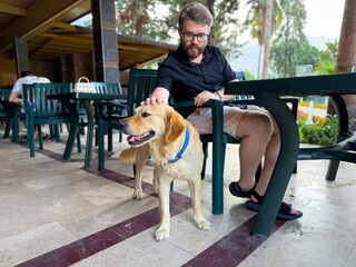 Man petting a golden dog with blue collar at outdoor table. Friendship, companionship and leisure...