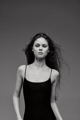 Fototapeta premium Black and white portrait of a serious young woman with long hair wearing a black dress against dark background