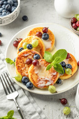 Cottage cheese pancakes with berries, mint leaves and condensed milk. Homemade dessert syrniki for healthy breakfast close up