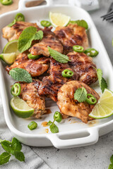 Spicy grilled chicken thighs roasted with chilli and lime on white dish close up, light gray kitchen background