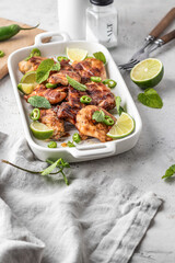Spicy grilled chicken thighs roasted with chilli and lime on white dish, light gray kitchen background