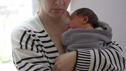 Mother holding sleeping newborn against her chest, wrapped in a cozy blanket, showcasing a tender...