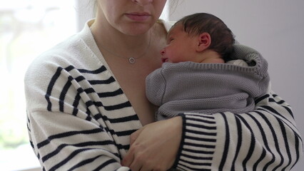 Mother holding sleeping newborn against her chest, wrapped in a cozy blanket, showcasing a tender...