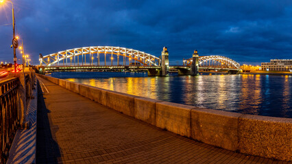 Night panorama of illuminated Bolsheokhtinsky Bridge with reflection in Neva River and granite embankment. Saint Petersburg, Russia.