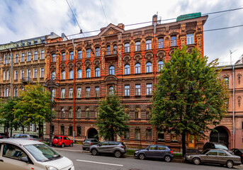Fototapeta premium Ornate eclectic style tenement house facade with stucco decorations, arched windows and autumn trees. Saint Petersburg, Russia.