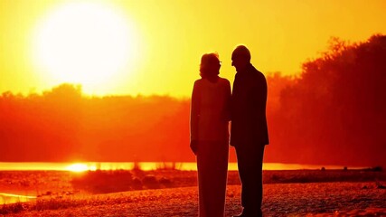 Senior couple silhouette holding hands and talking on a shoreline with a bright golden sunset in the background. Representing a peaceful retirement and financial security, enjoying golden years.
