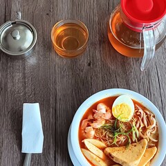 Overhead shot of a bowl of noodle soup with shrimp and egg, tea, and a sugar bowl.