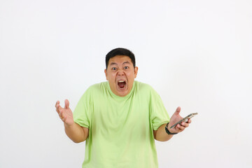 Fototapeta premium Young Asian man holds phone with furious face and annoyed gestures clearly.